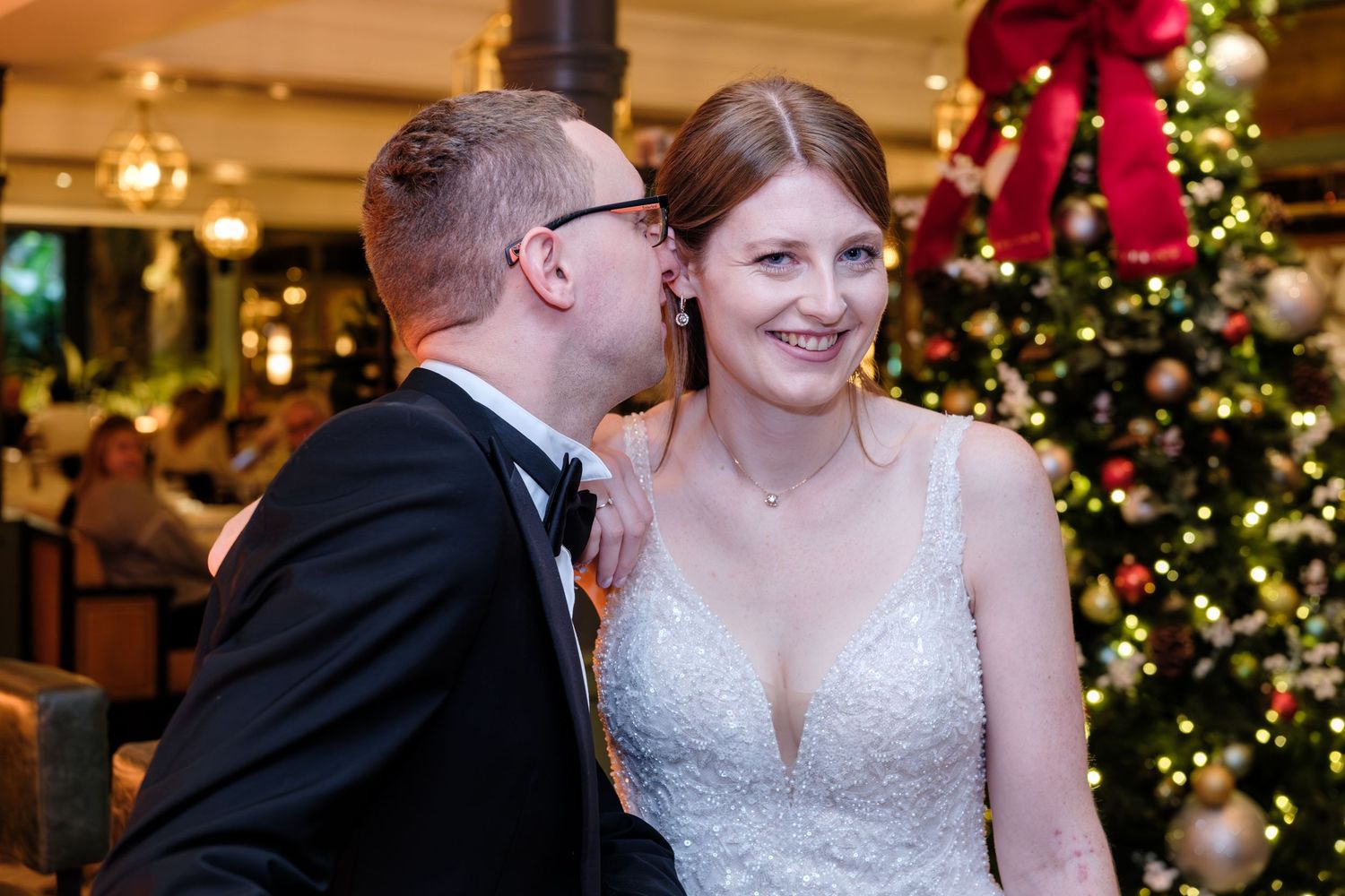 A couple shares a romantic moment during their winter wedding celebration with decorated Christmas trees in the background.