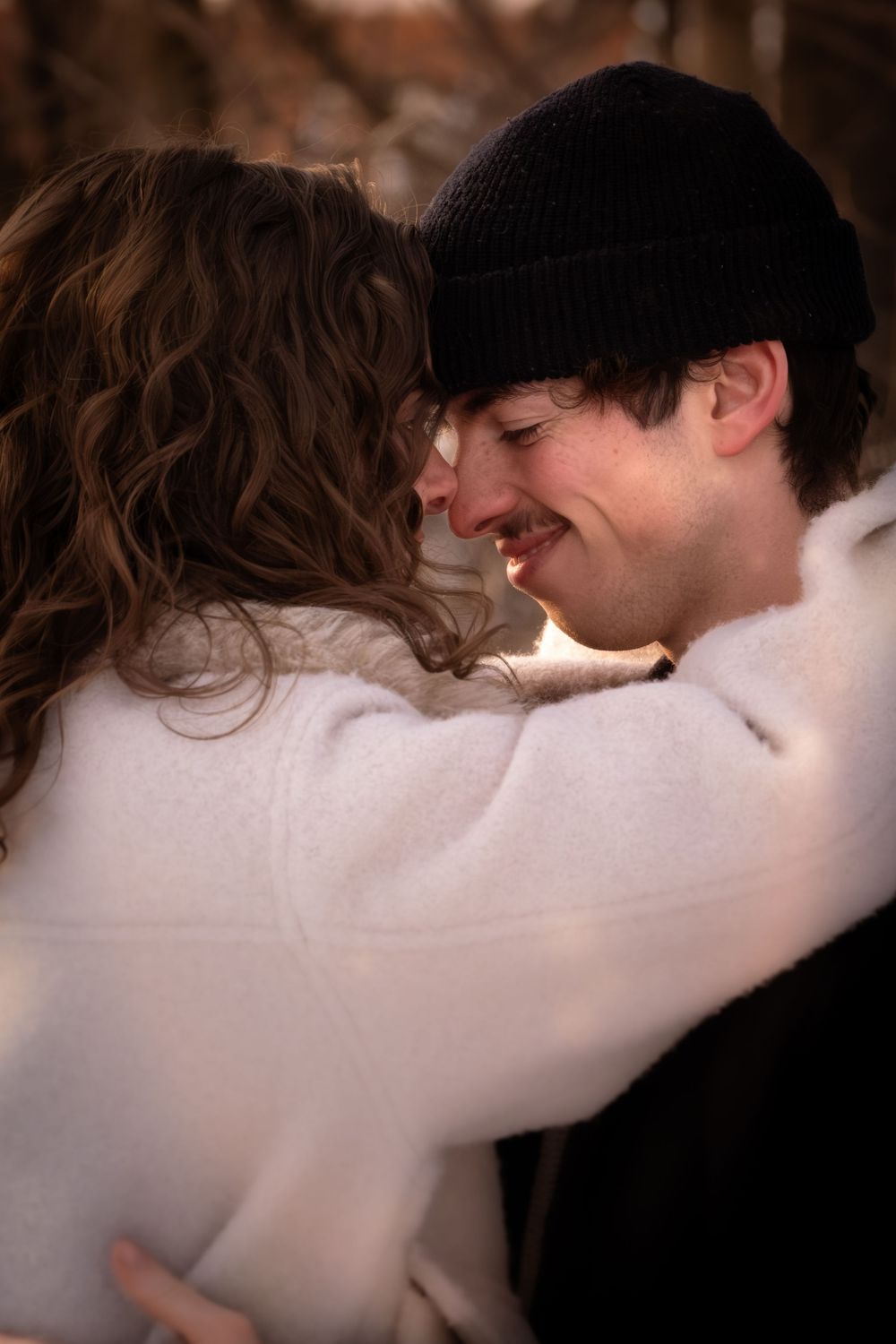 A tender romantic moment between a couple embracing outdoors, with one wearing a black beanie and the other in white.