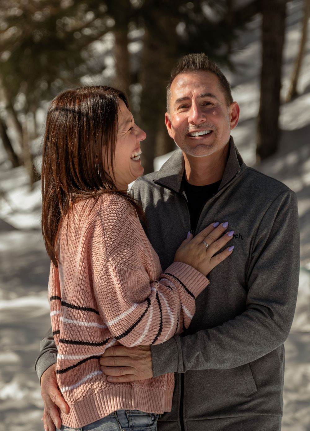 A couple shares joyful laughter together during a winter photoshoot in the snowy woods.