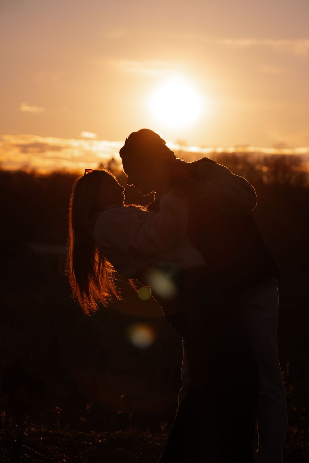 Romantic couple silhouette kissing against a golden sunset sky with warm orange hues and soft lens flare.
