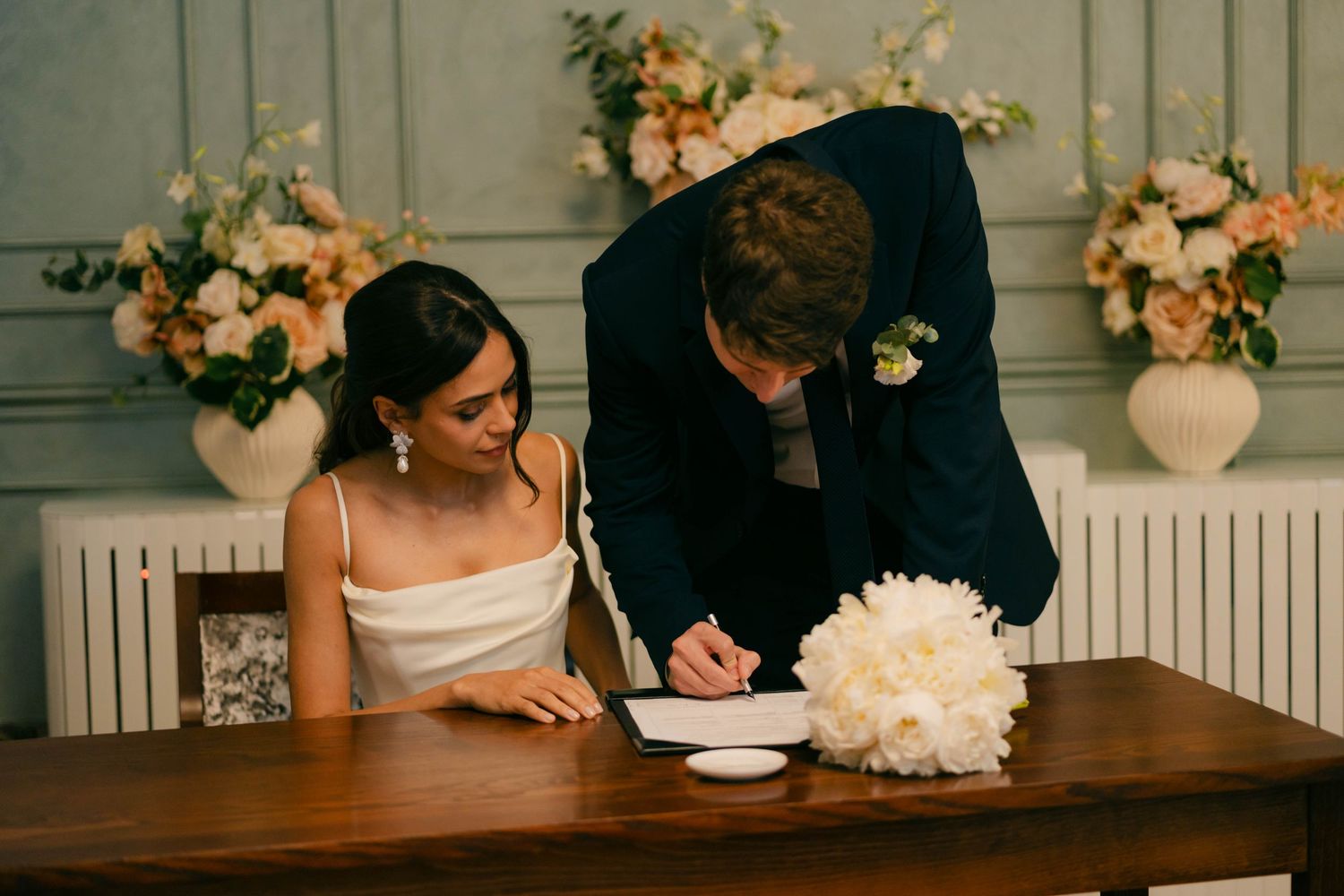 Wedding couple signing documents at an elegant indoor venue with floral decorations.