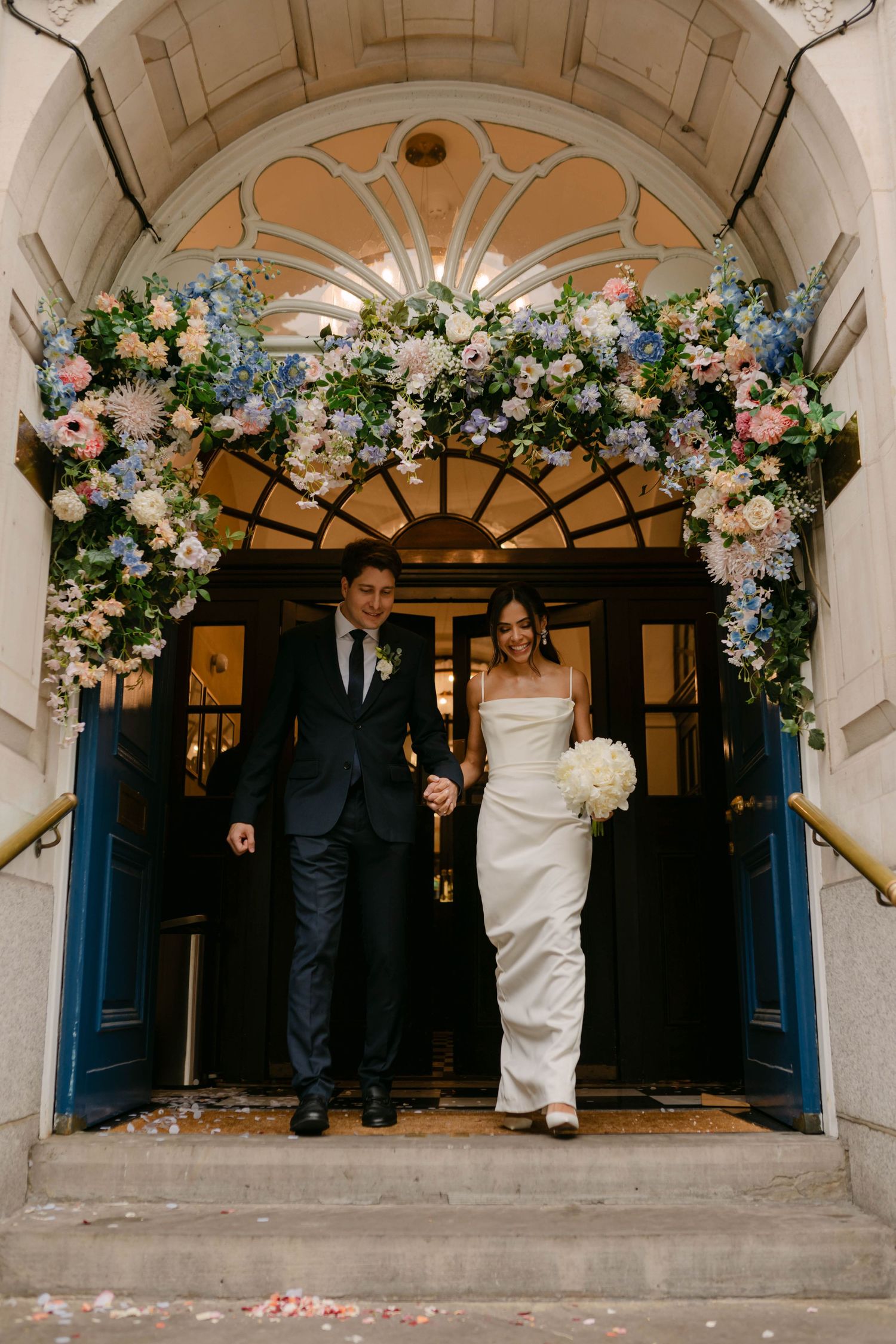 Wedding couple standing under a stone archway decorated with pink and white floral arrangements.
