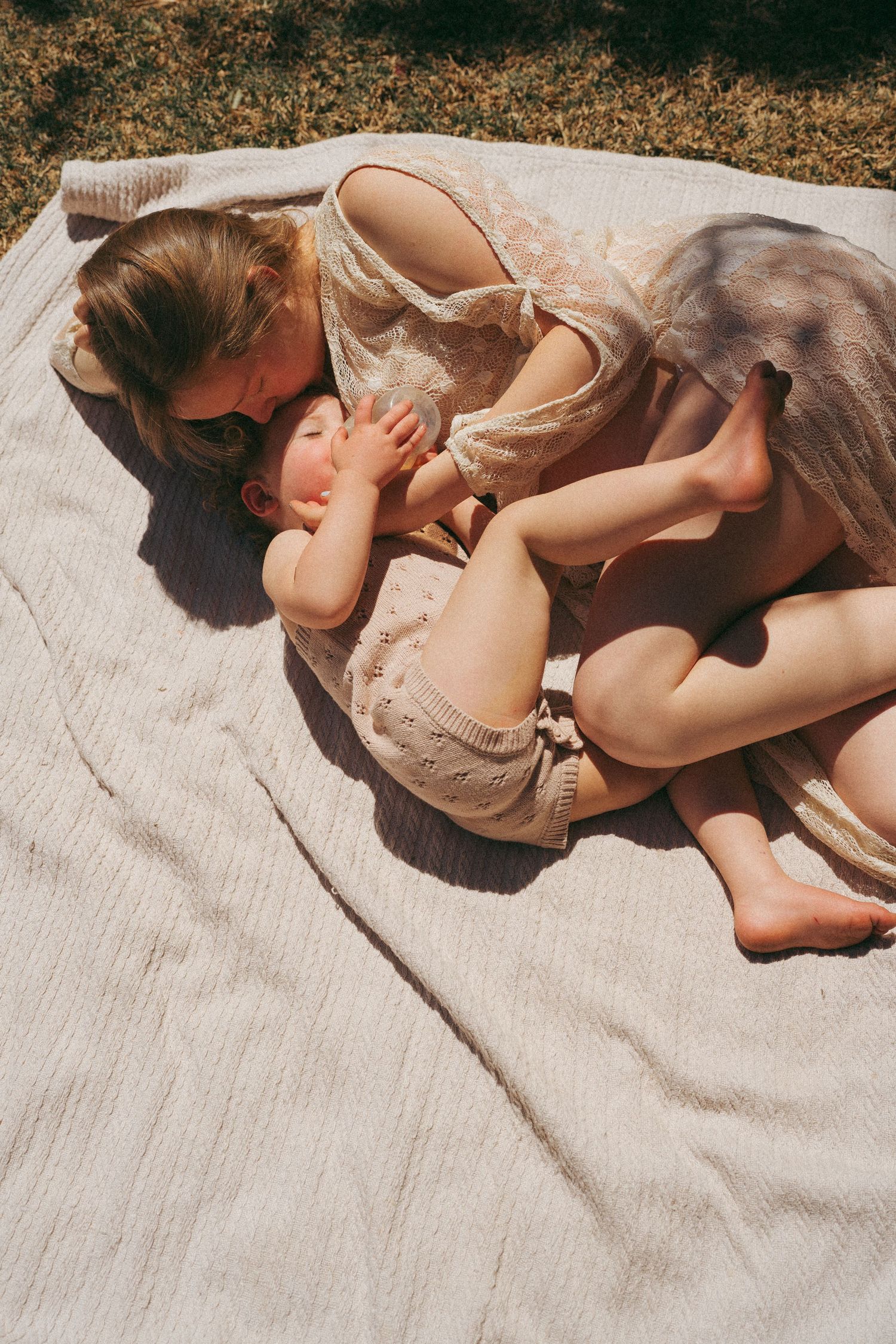 A tender moment between parent and child laying on a blanket outdoors.