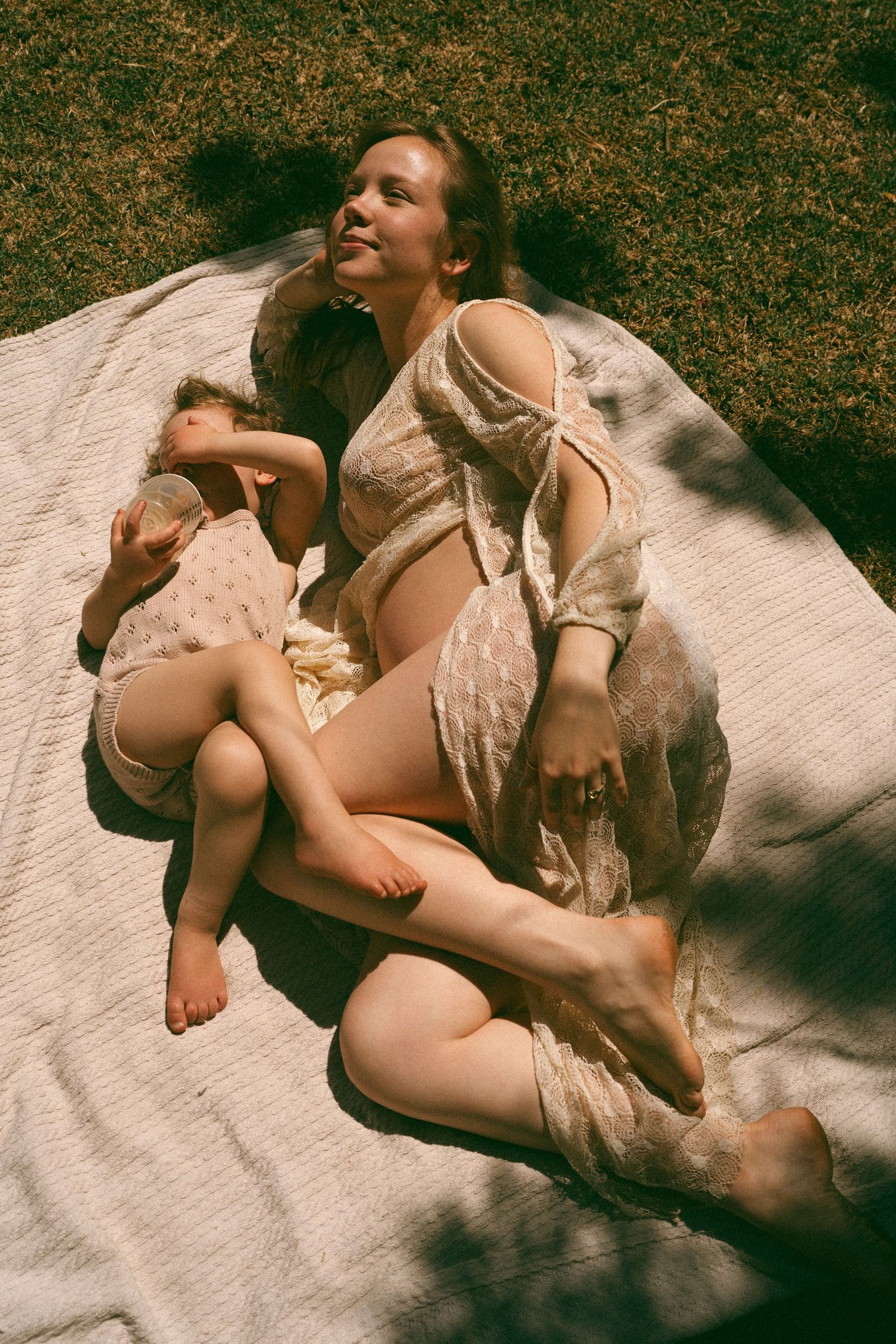 Two figures resting on a white blanket in dappled sunlight.