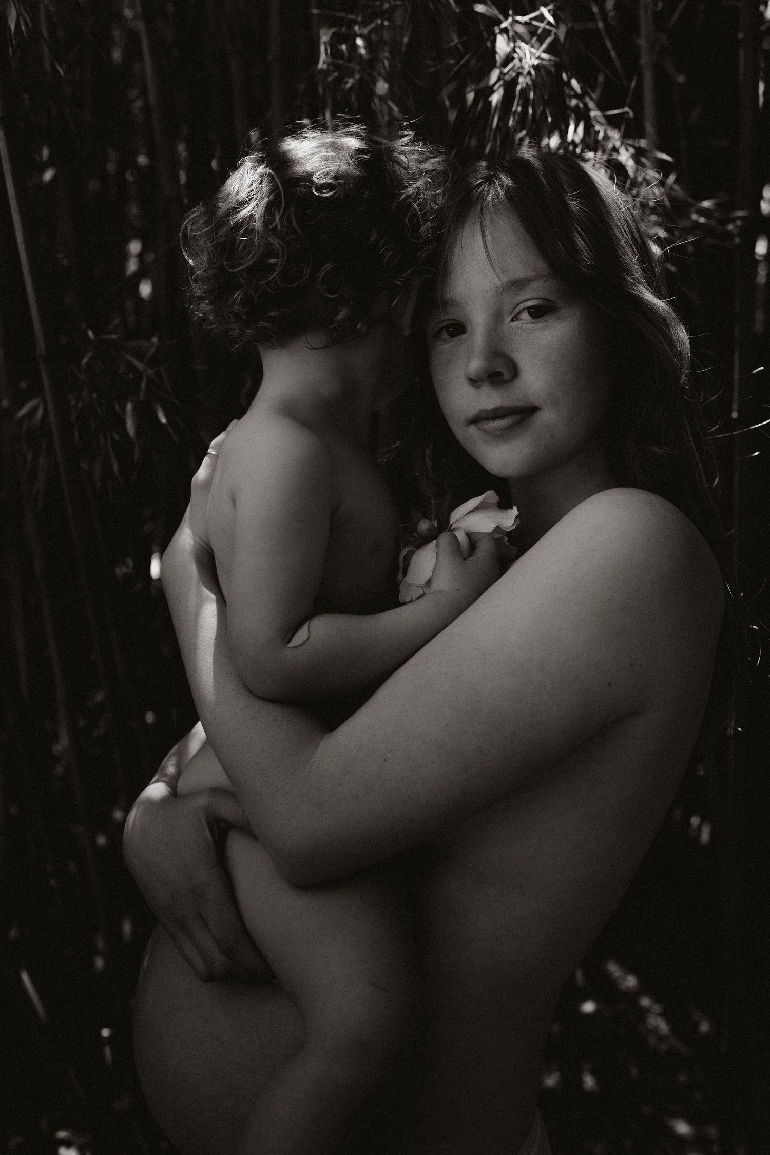 Black and white artistic portrait showing tender embrace against natural backdrop.