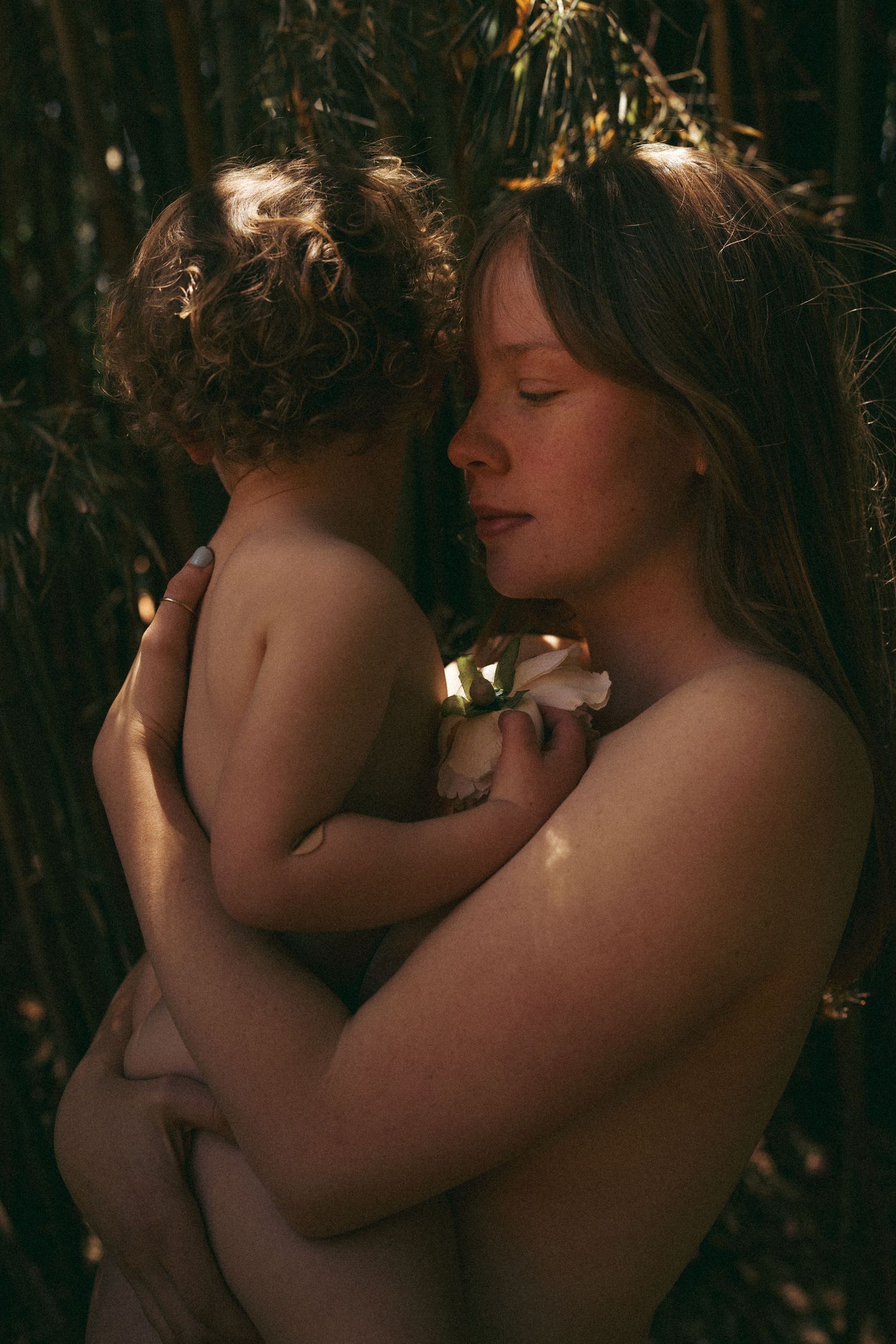 Intimate portrait showing gentle embrace in natural setting with filtered light.