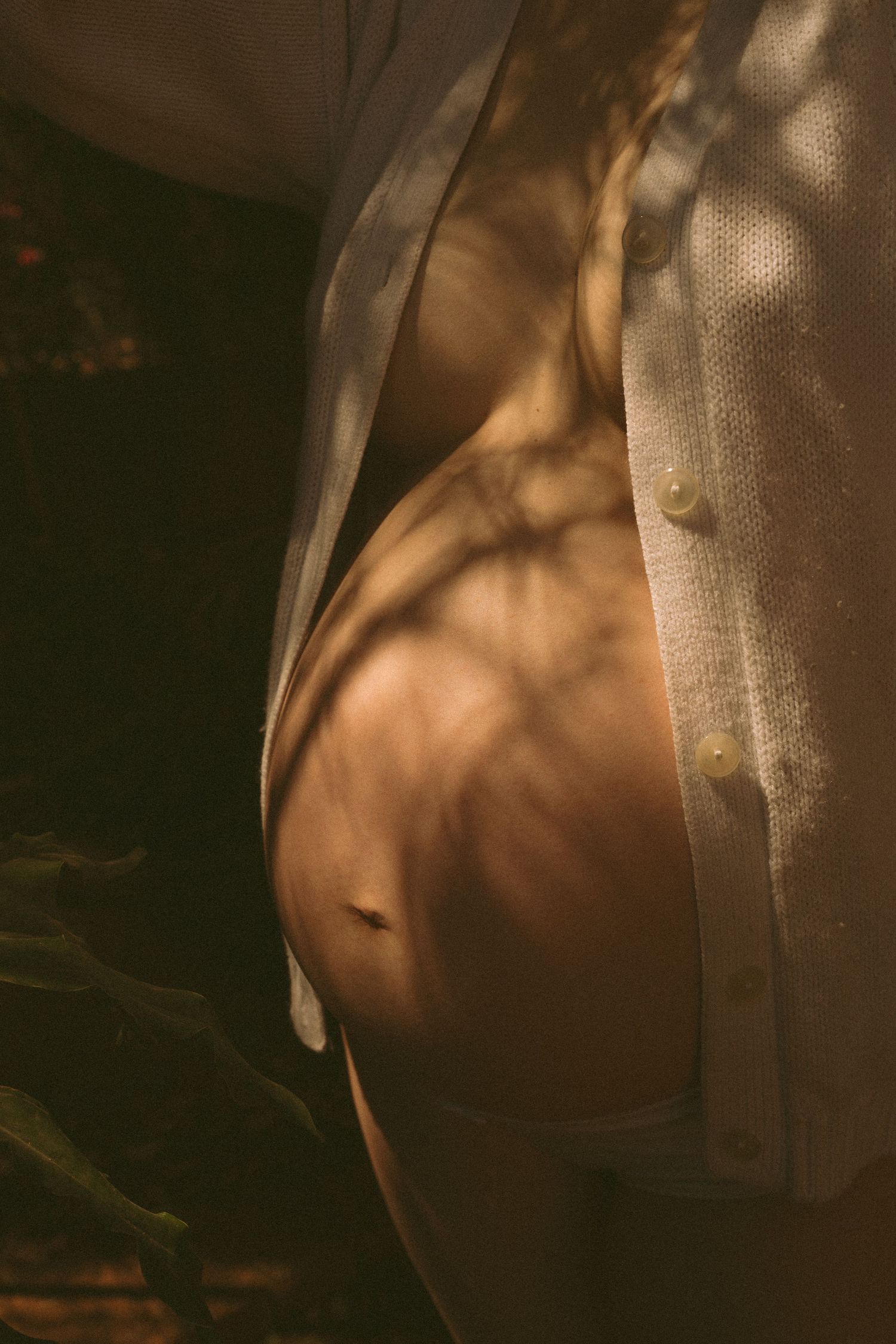 Artistic close-up sequence of a bare pregnant belly in warm lighting with shadows and fabric draping across it.