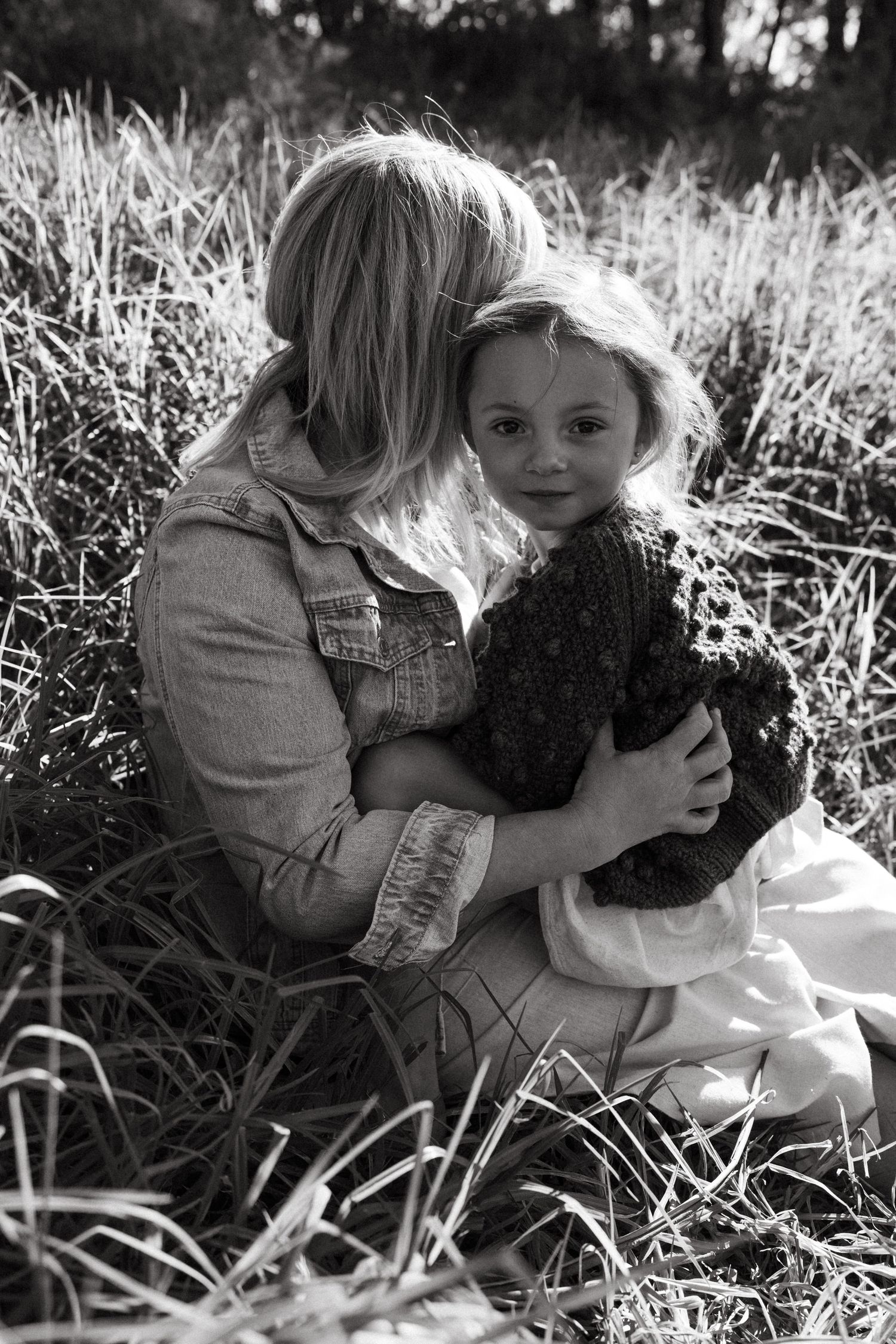 A black and white photo shows two people embracing in tall grass.