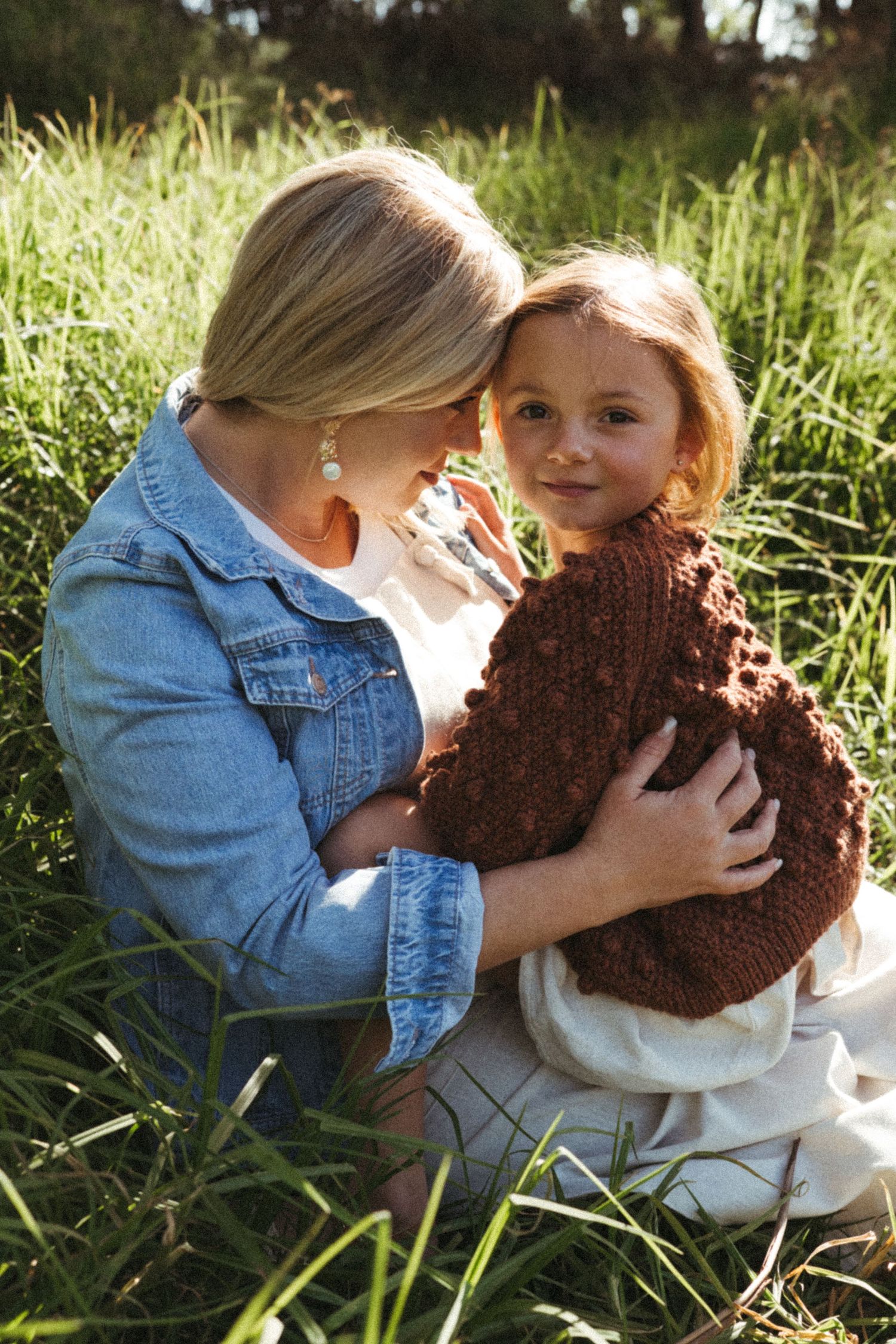 People share an intimate moment in a grassy field while holding a brown knitted object.