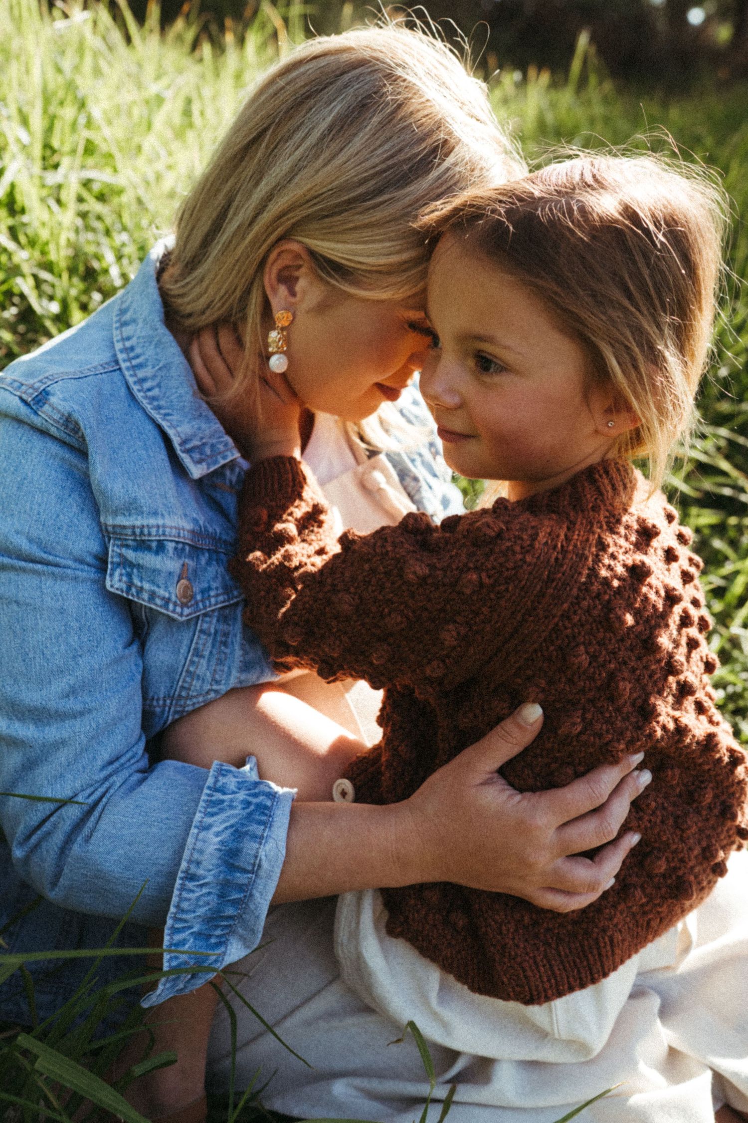Two people share a close moment in sunlit grass while holding a brown knitted piece.