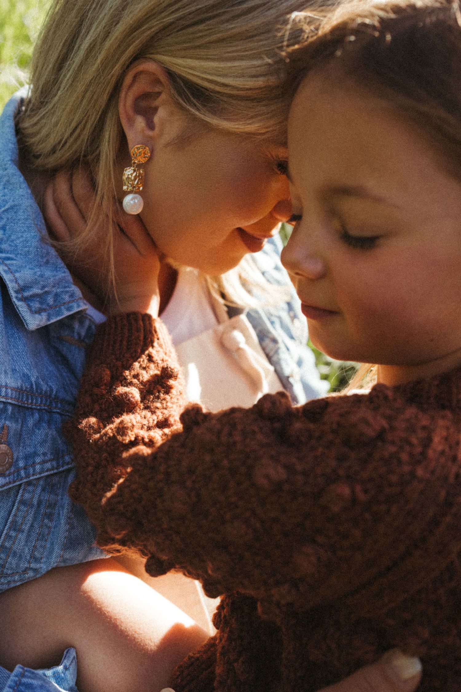 Sunlight filters through as two people share a close moment with a brown knitted item.
