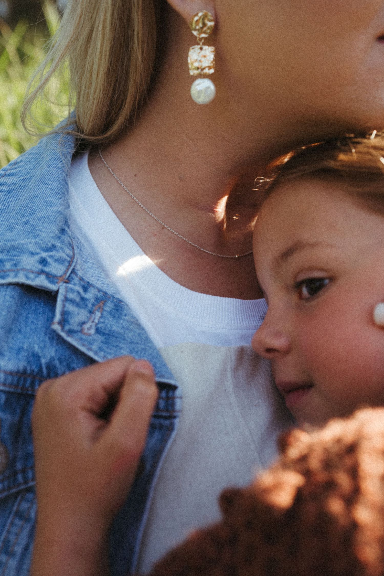 A close-up shot showing denim jacket and pearl drop earrings in natural sunlight.