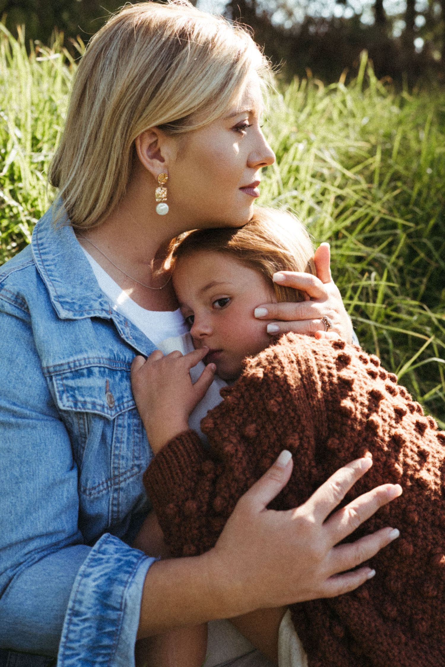 A tender moment captured outdoors with a brown knit sweater and denim jacket against tall grass.