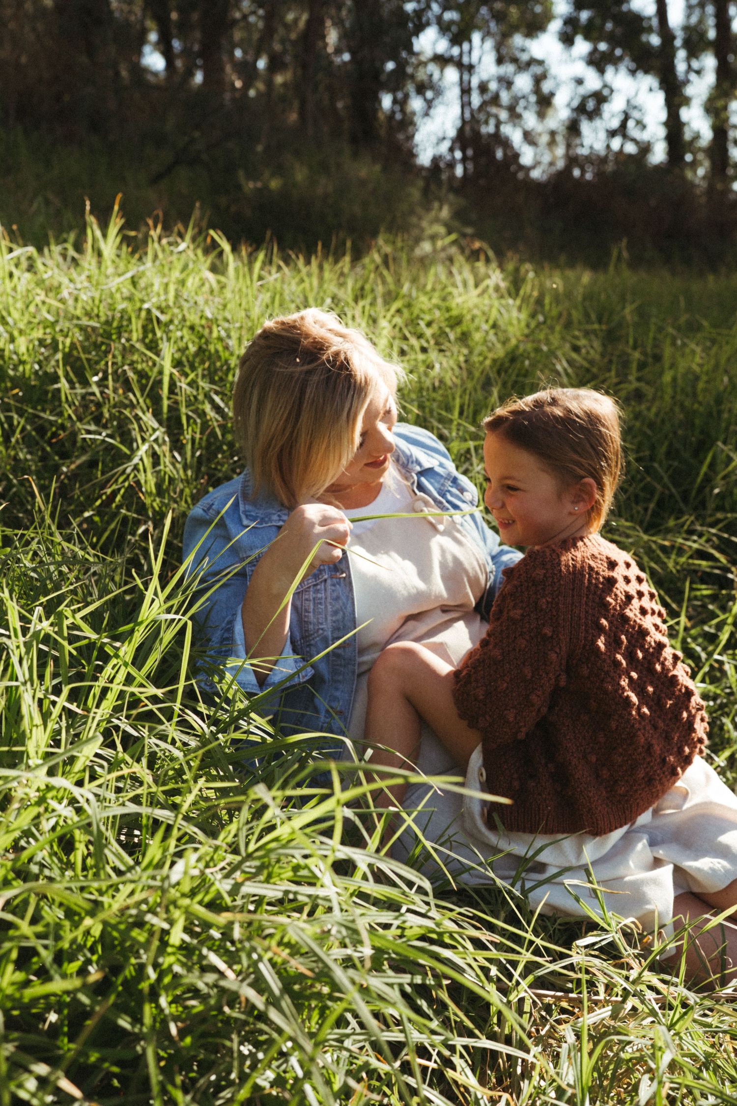 A warm sunlit moment shared between two people sitting in wild grass wearing casual attire.