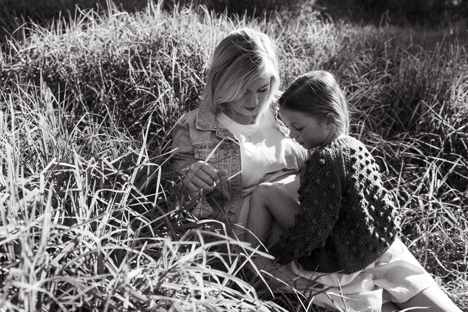 A black and white photograph of two people sharing an intimate moment in tall grass.