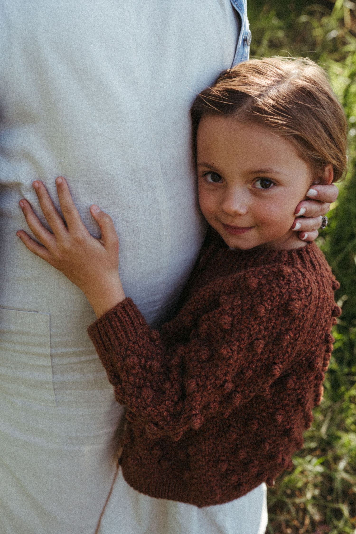 A sweet embrace showing a brown knit sweater against white clothing in natural lighting.