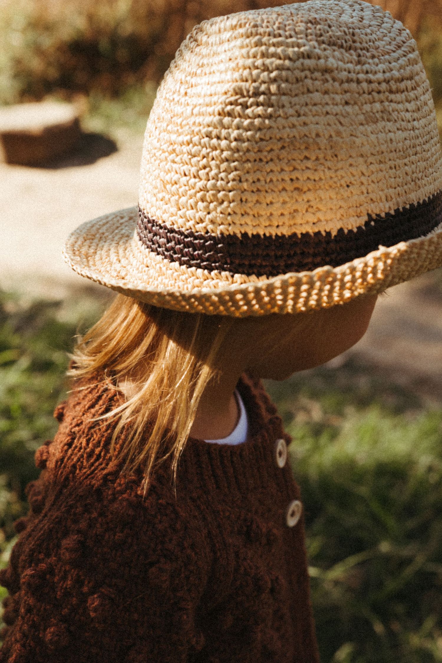 A straw fedora hat with brown band worn with a brown knit sweater in warm sunlight.