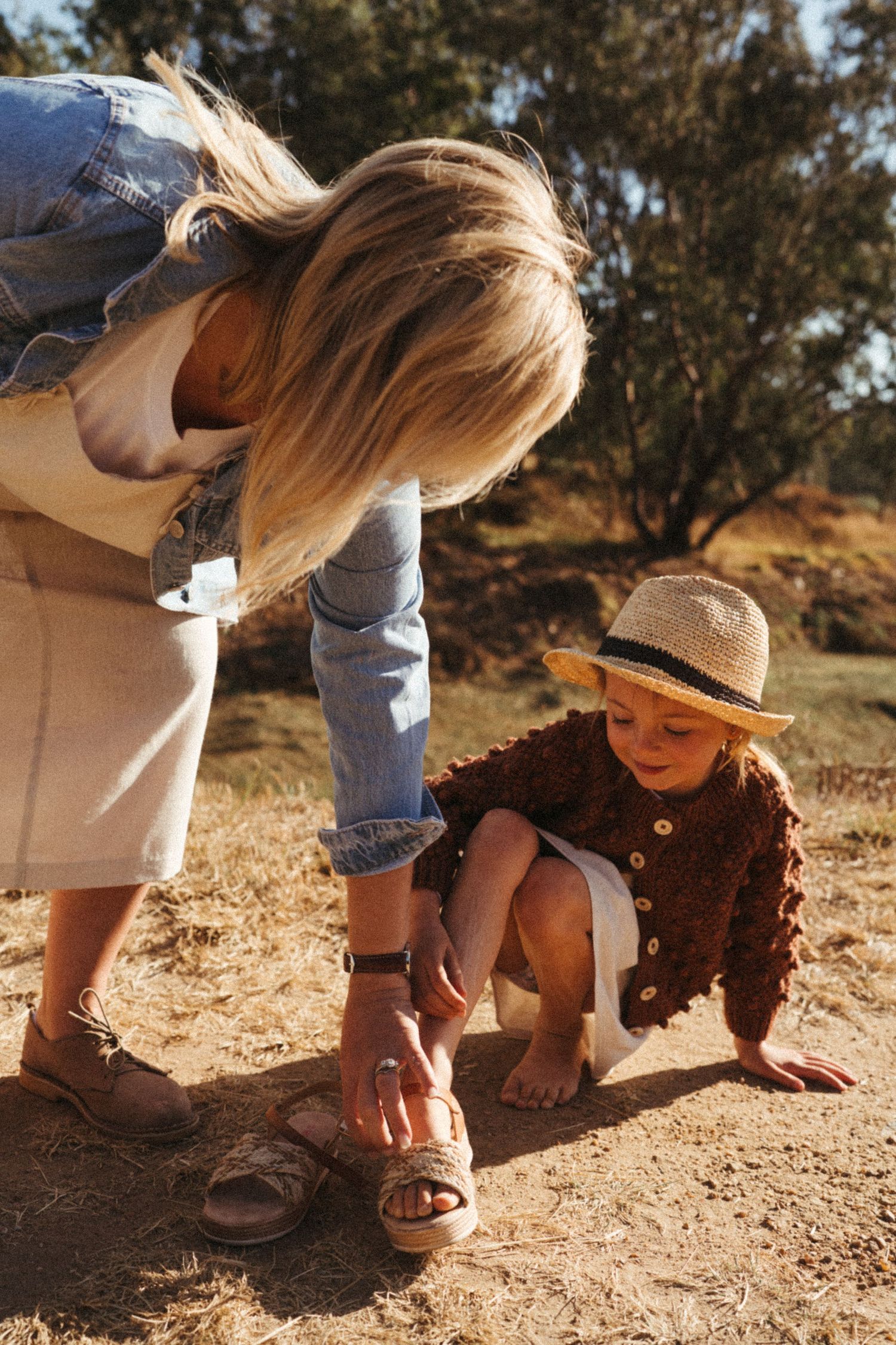 Helping adjust sandals on dirt path during sunny outdoor adventure.