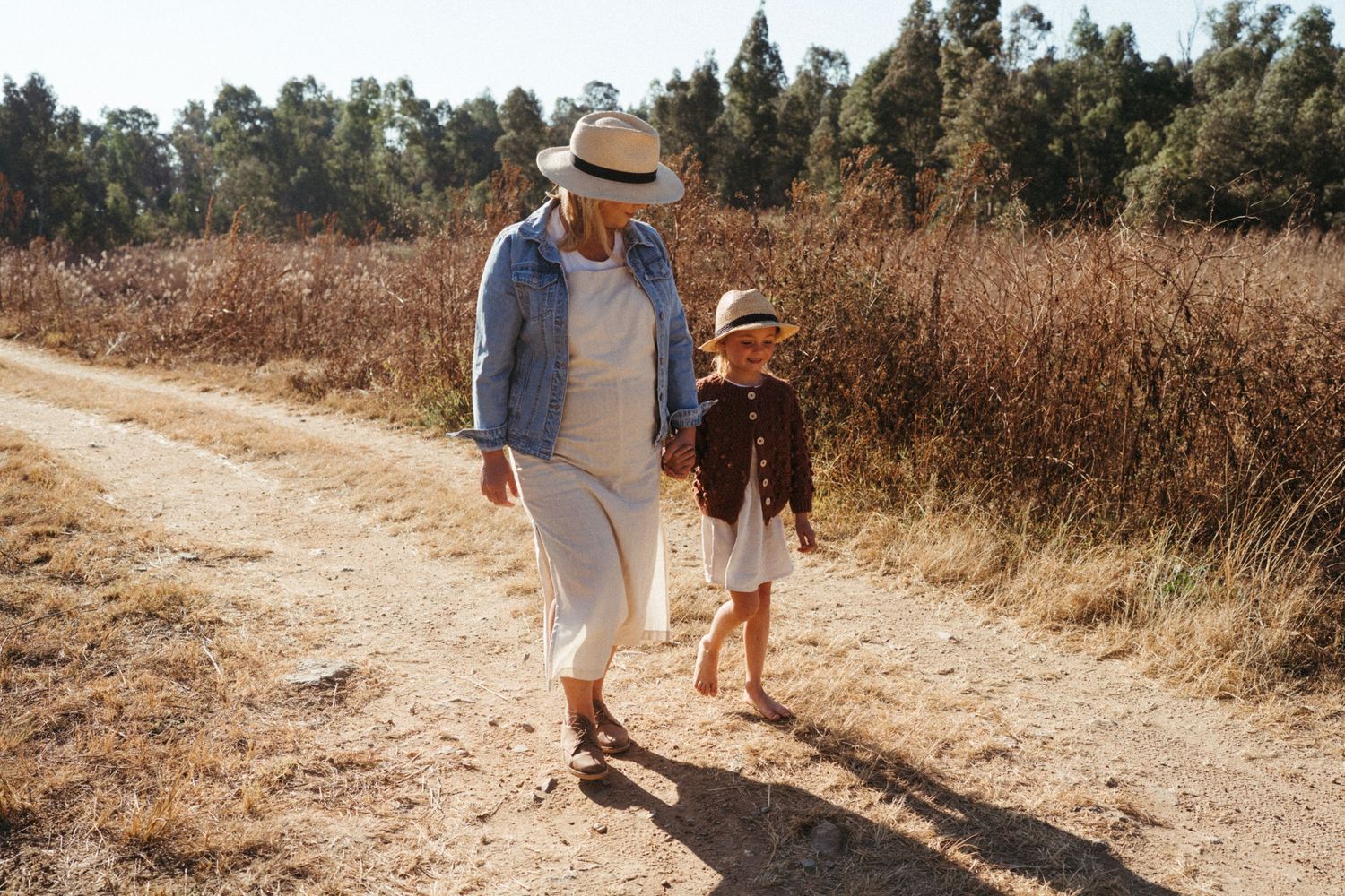 Two figures walking together on sunlit dirt path through dry grassland.