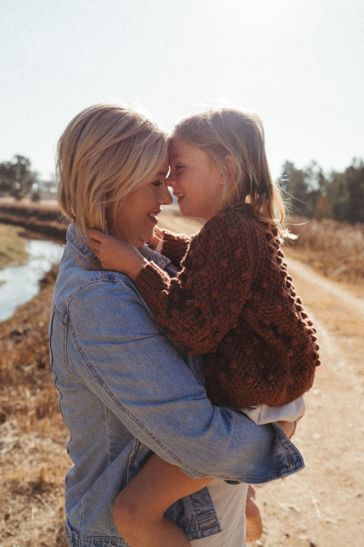 A sun-drenched moment of affection captured on a dirt path with natural scenery in the background.
