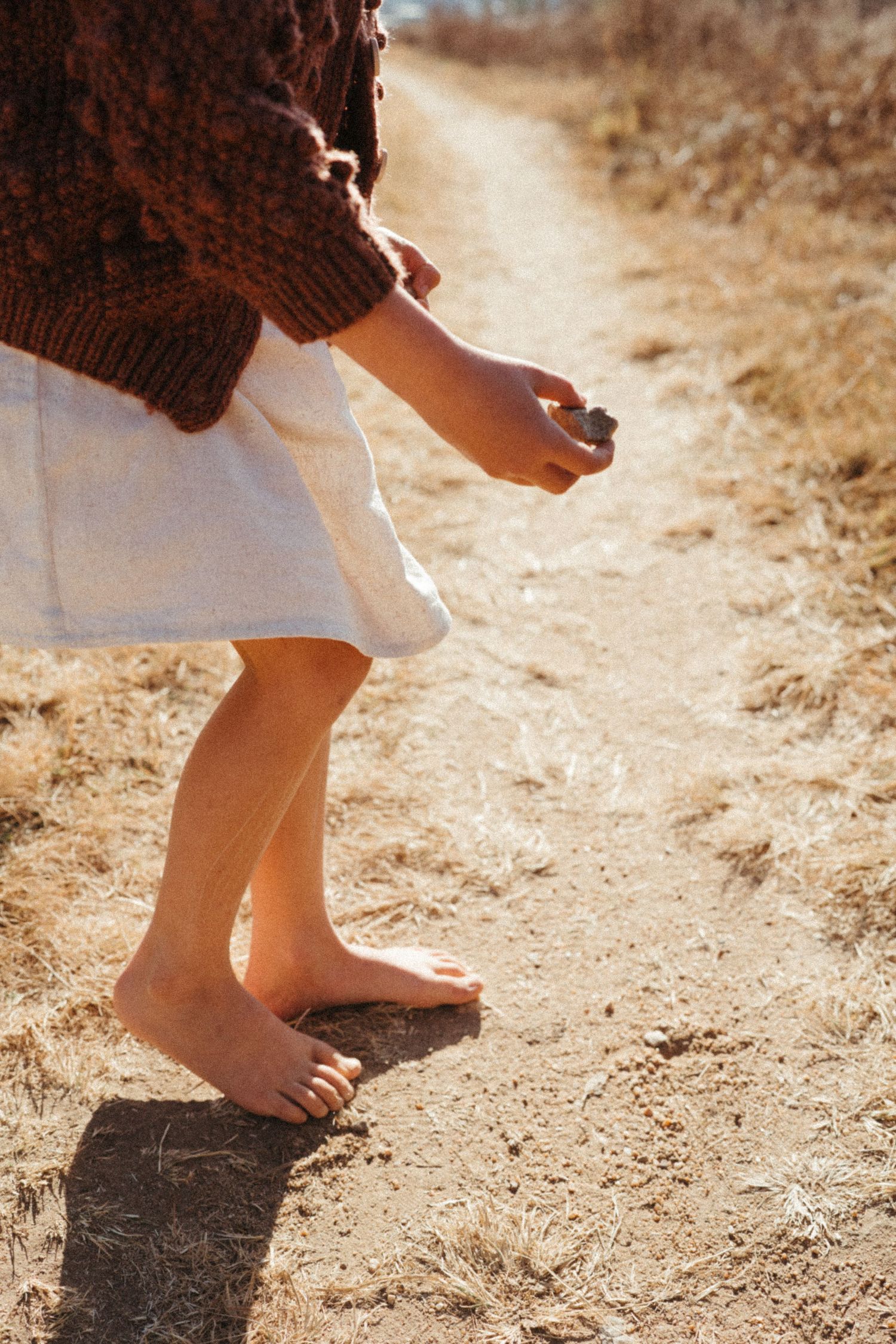 Close-up sequence of bare feet stepping on a sunlit dirt path.