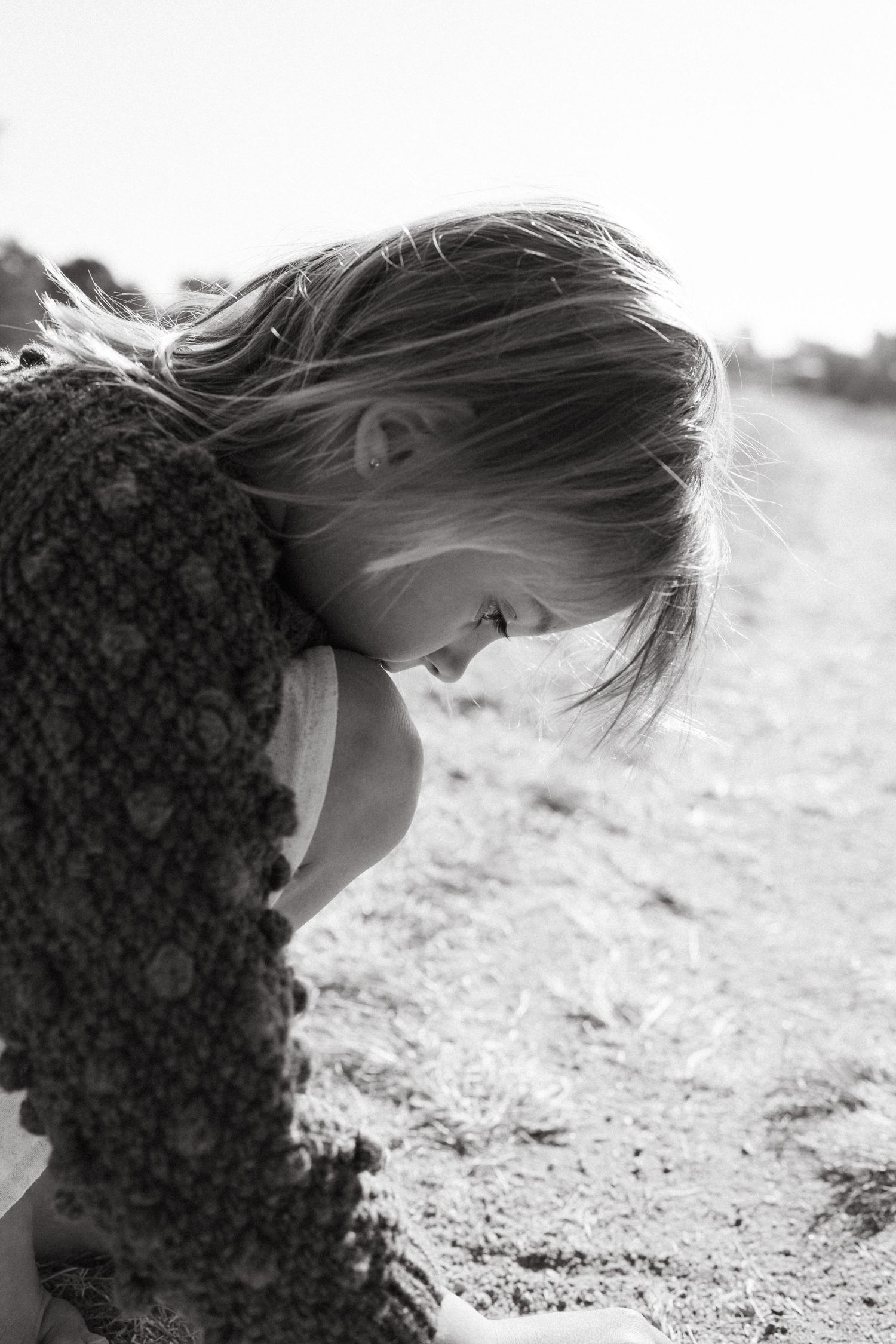 Side profile view of someone in a chunky knit sweater looking down at the ground.