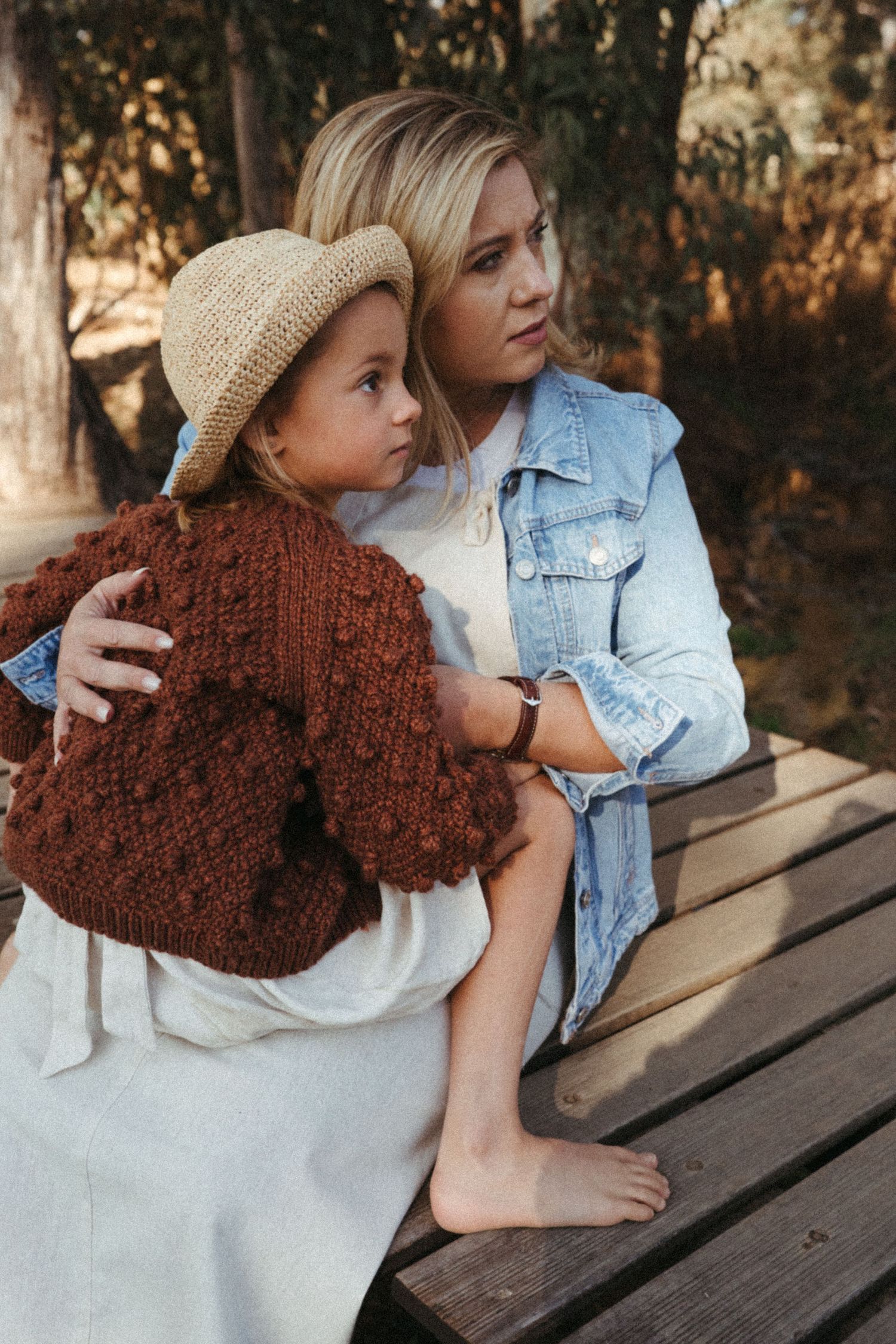 Two people sit together on a wooden bench wearing casual clothing and sharing an intimate moment.