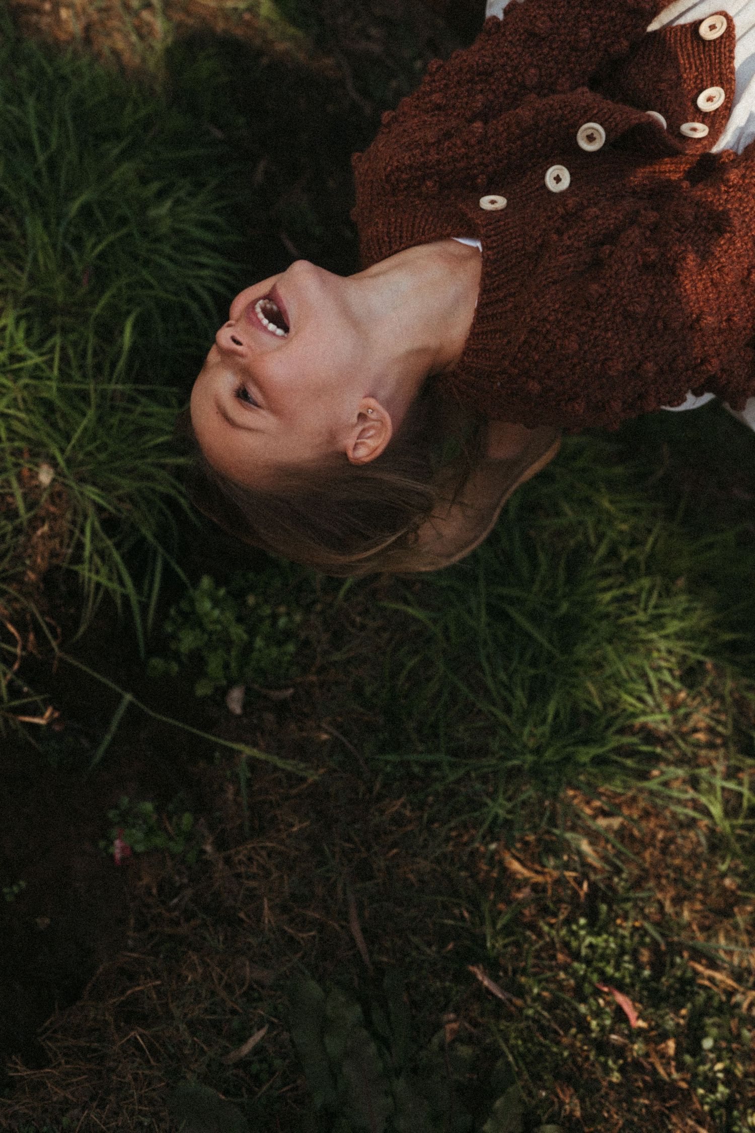Artistic portrait series showing someone lying in grass wearing a brown knit sweater.