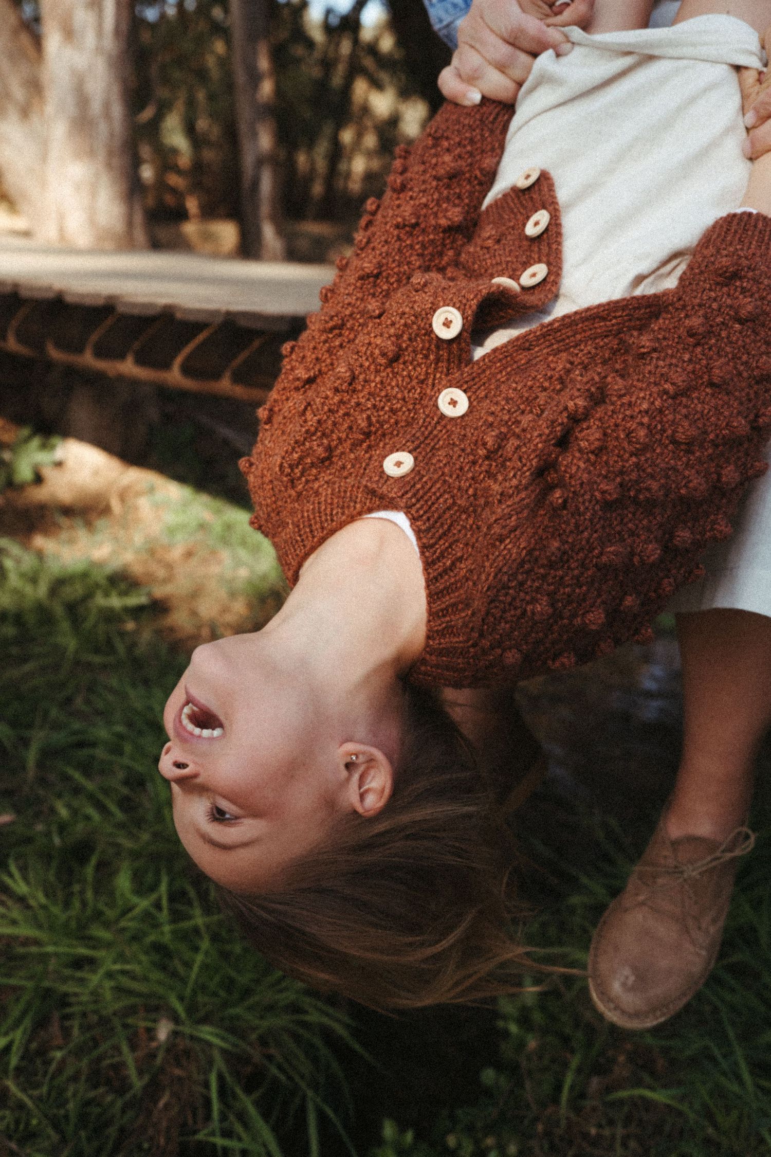 Dynamic angles capture someone wearing a brown buttoned sweater lying in grass.