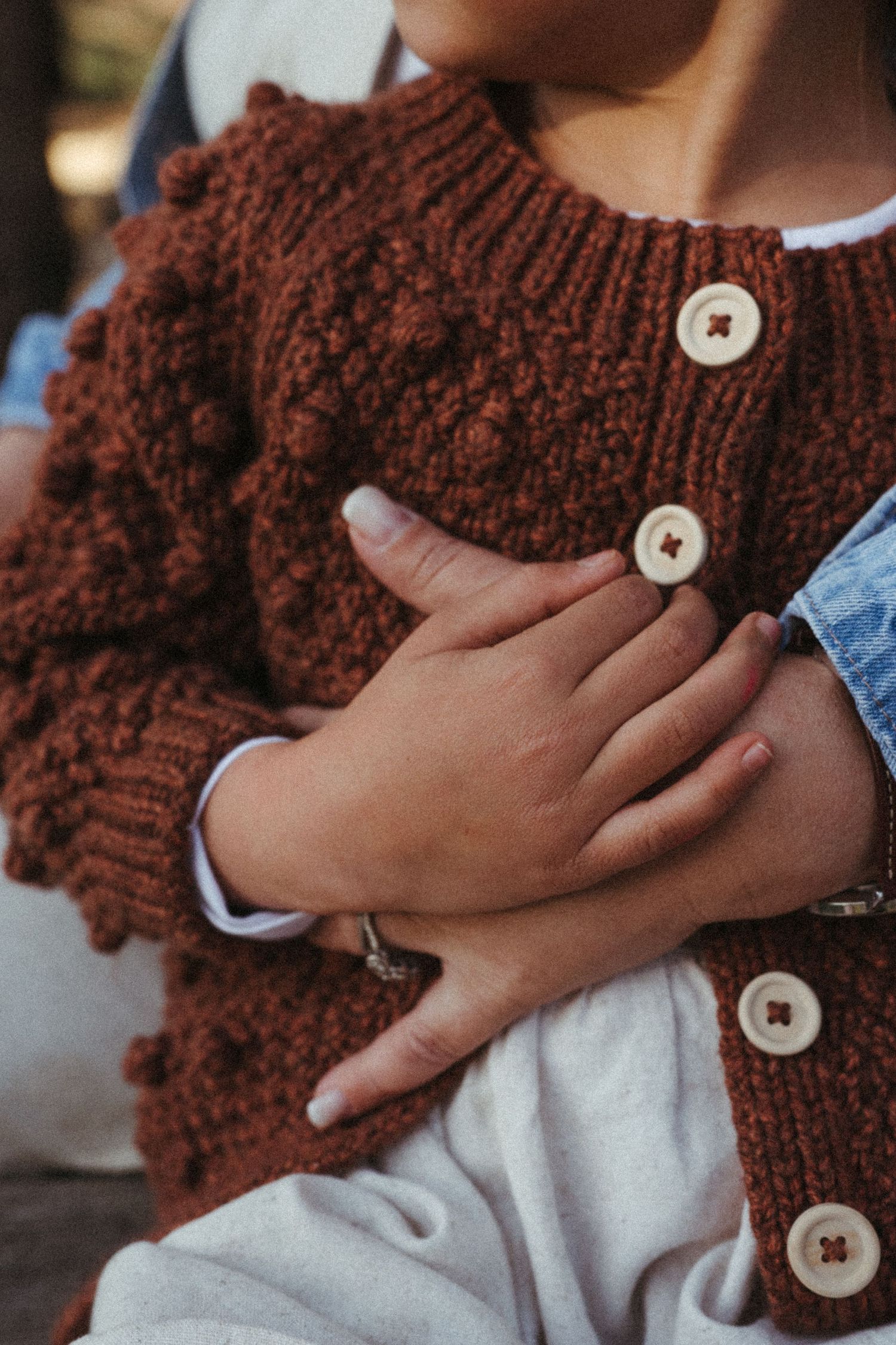 Detail shots of hands touching a brown knitted scarf with decorative buttons against white clothing.