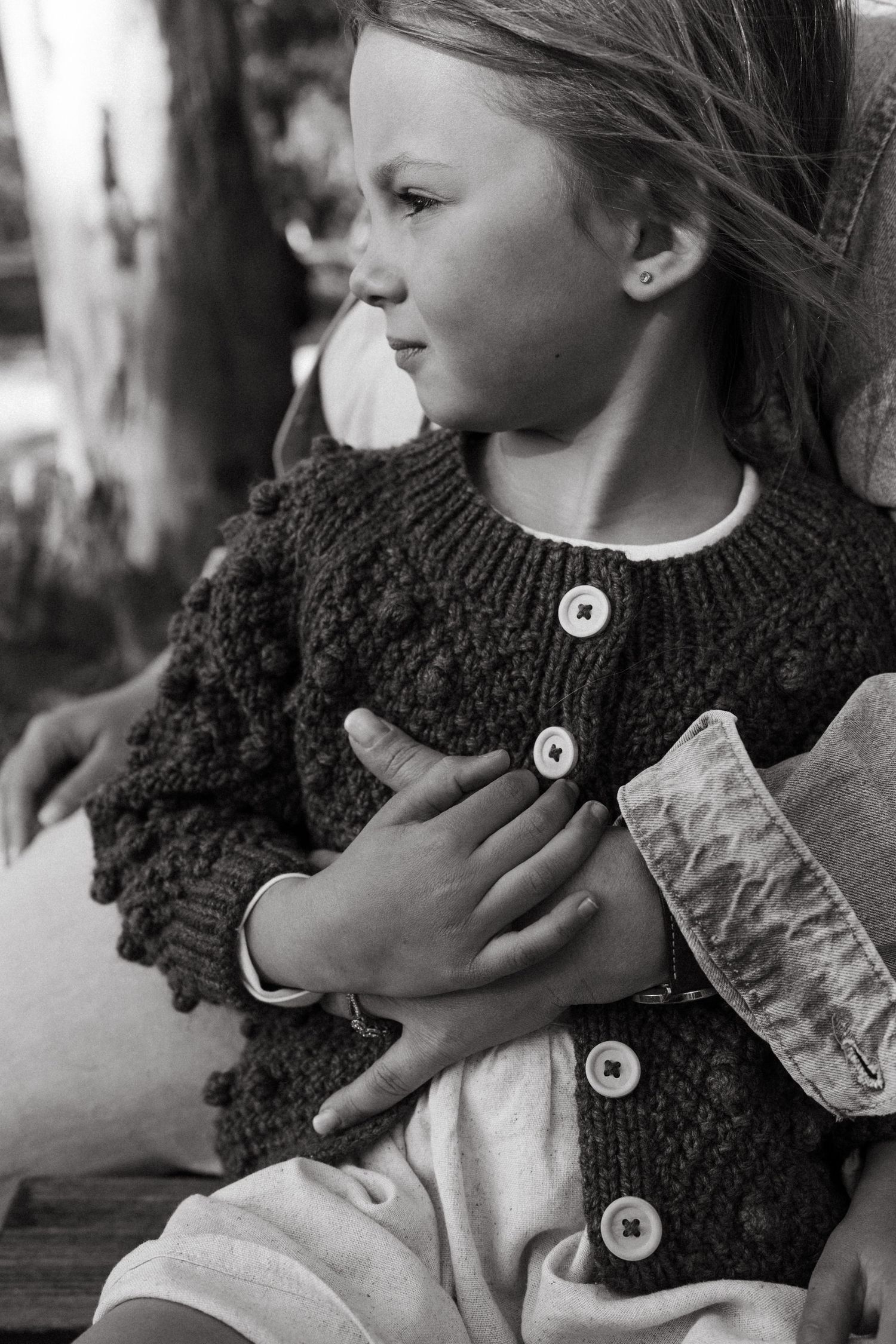 Black and white series showing details of a textured knit scarf with buttons in natural lighting.