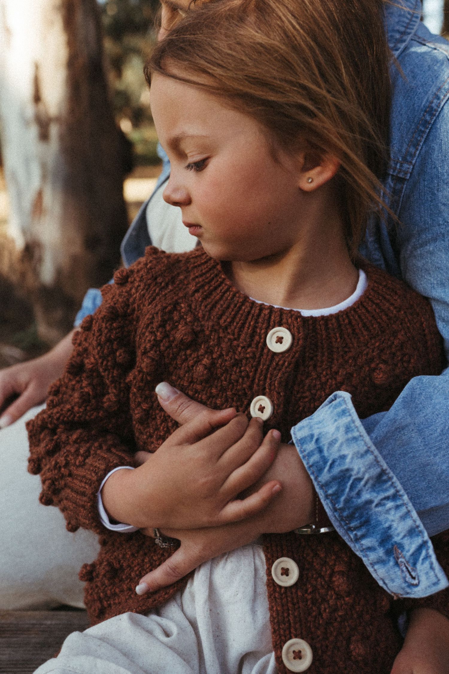 Multiple angles of a brown knit scarf with buttons worn with denim and white clothing outdoors.