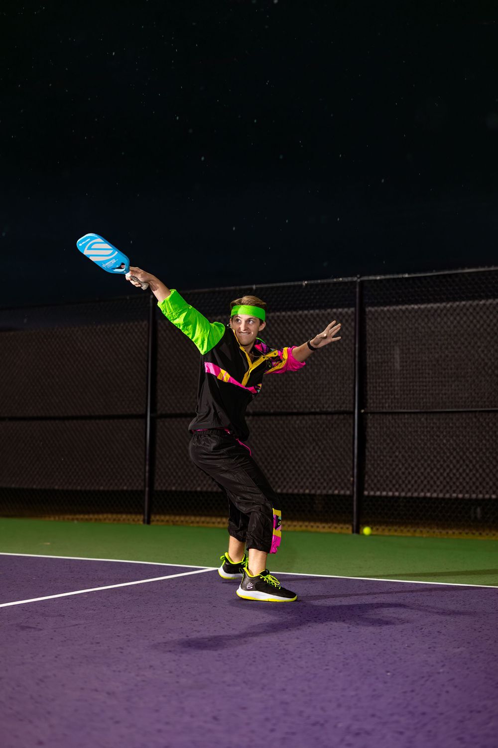 Dynamic sequence shows a person performing acrobatic moves in neon clothing on a purple tennis court at night.