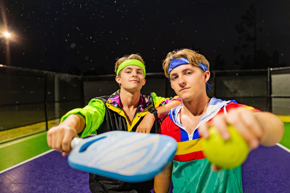 Athletes in bright sportswear pose together on a purple tennis court under night lights.