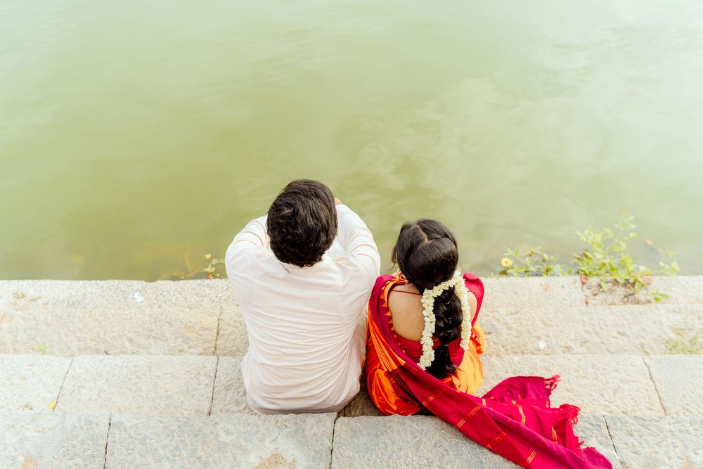 Two people sit together on stone steps beside a tranquil lake.