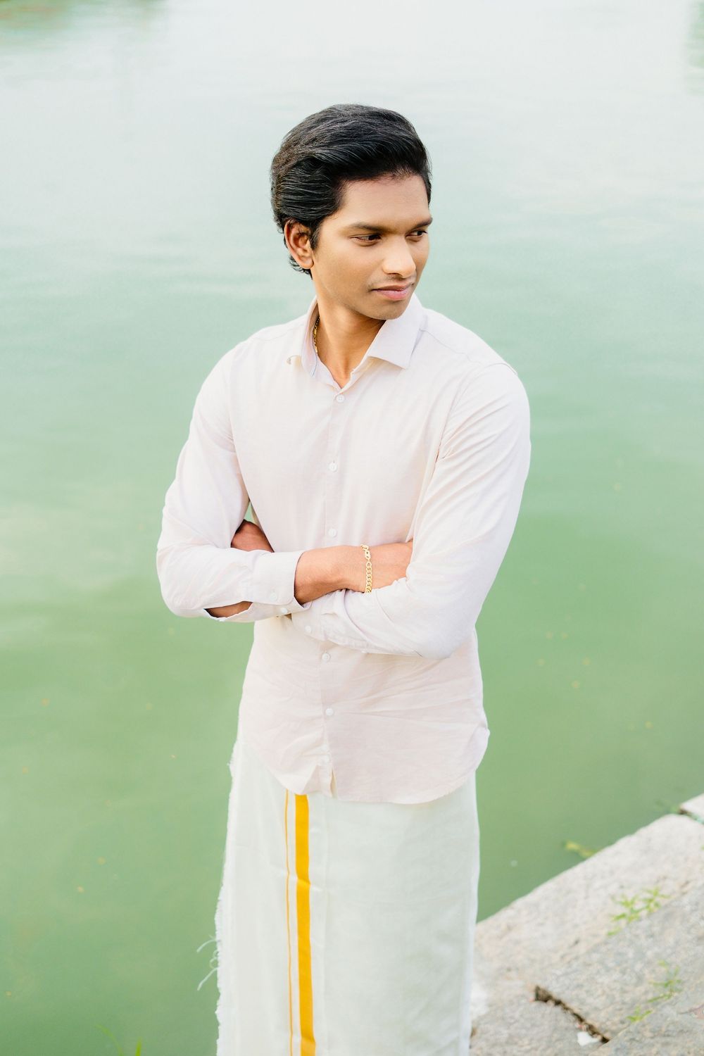Person in white formal shirt poses thoughtfully against serene waterfront background.