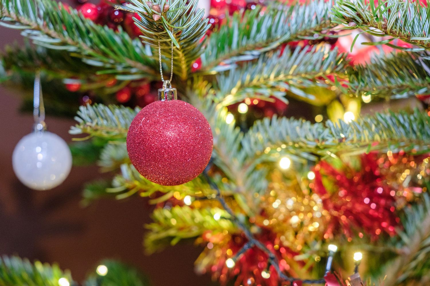 Closeup of a decorated Christmas tree with red and silver ornaments, pine branches, and warm glowing lights.