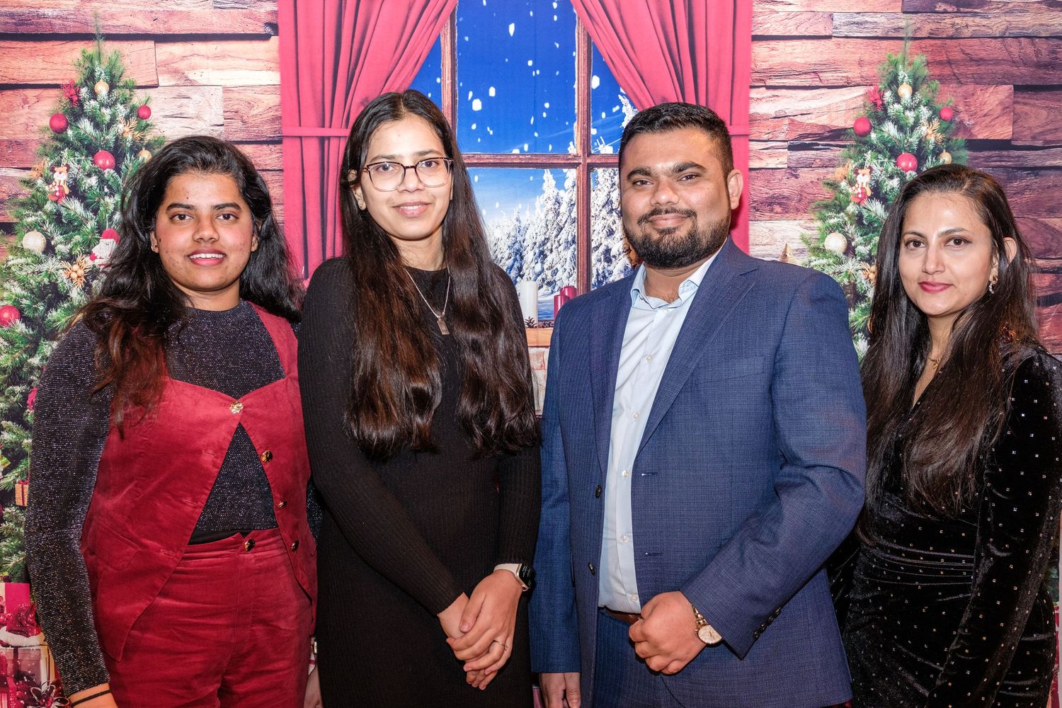 A group of friends poses together at a festive event with pink curtains and wooden wall backdrop.