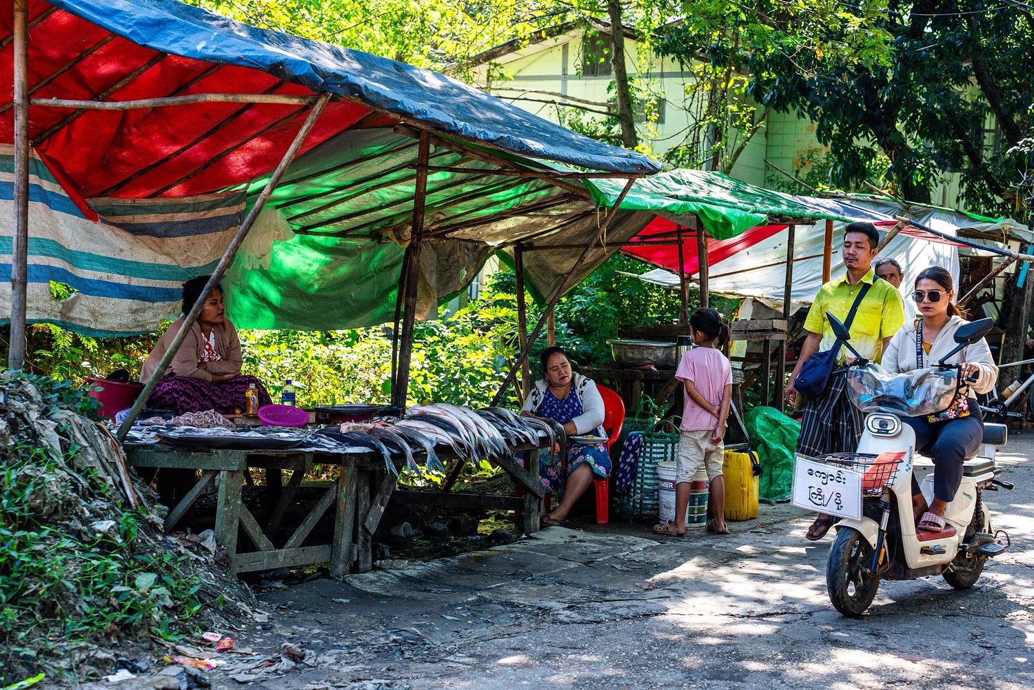 Colorful tents and tarps create a makeshift shelter area in a wooded outdoor setting.