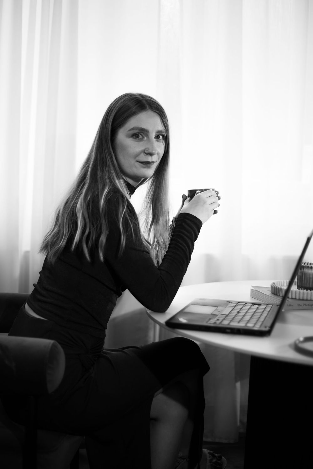 Person in black sweater sitting at desk with laptop and coffee in monochrome setting.Hypnotherapy at Huddle Studio Plymouth