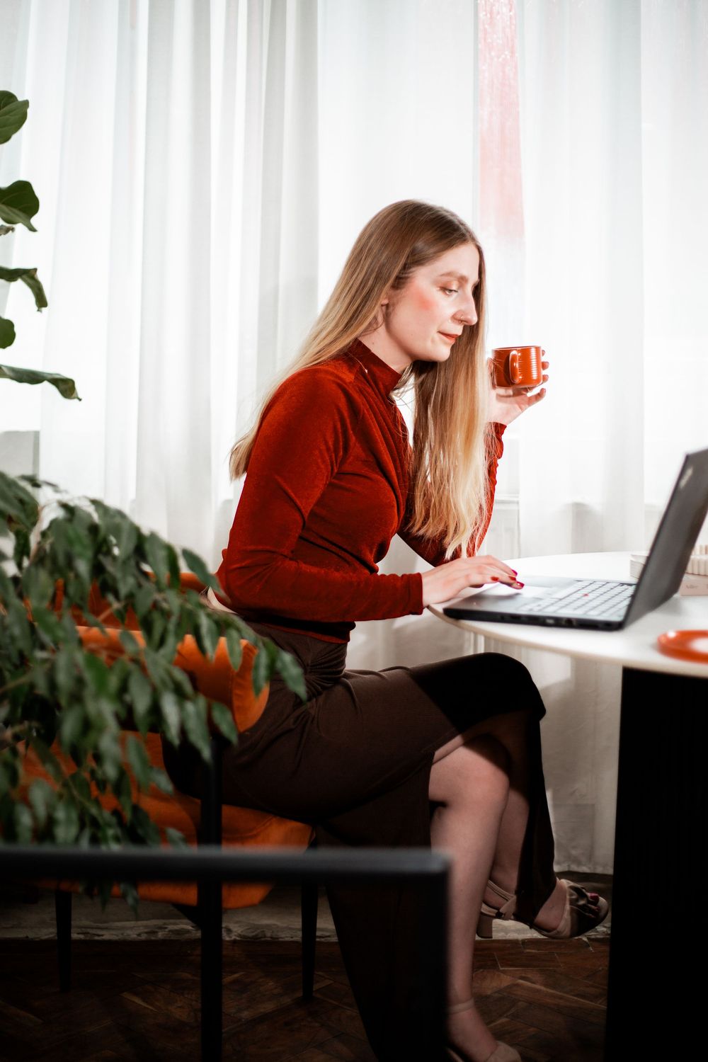 Woman in burgundy sweater working on laptop in bright office space.Hypnotherapy at Huddle Studio Plymouth