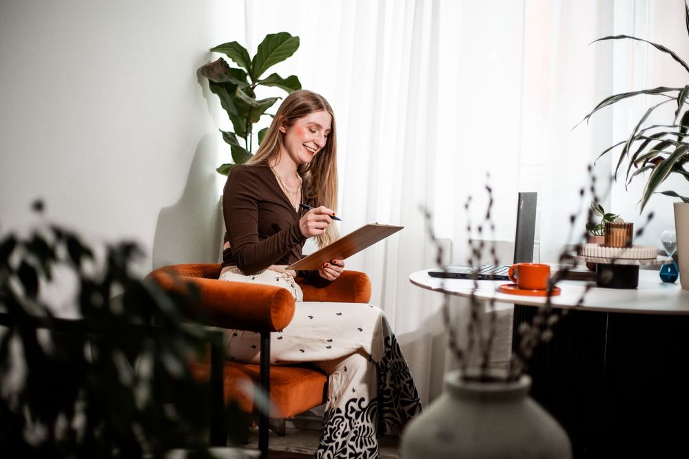 Person relaxing in brown sweater while reading and taking notes in a cozy home office with plants.Hypnotherapy at Huddle Studio Plymouth