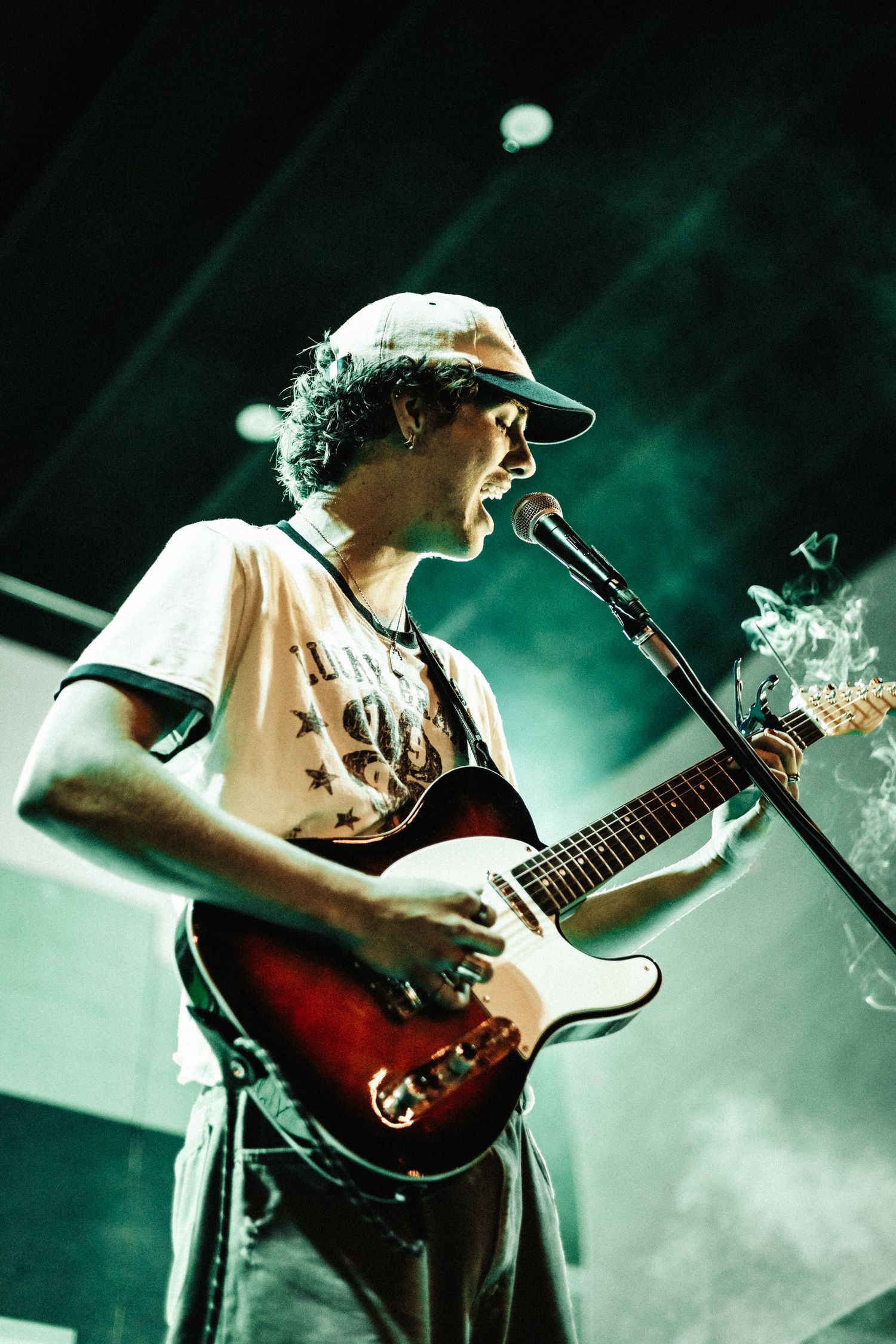 A guitarist performs on stage bathed in atmospheric green lighting and fog effects during a live concert performance.