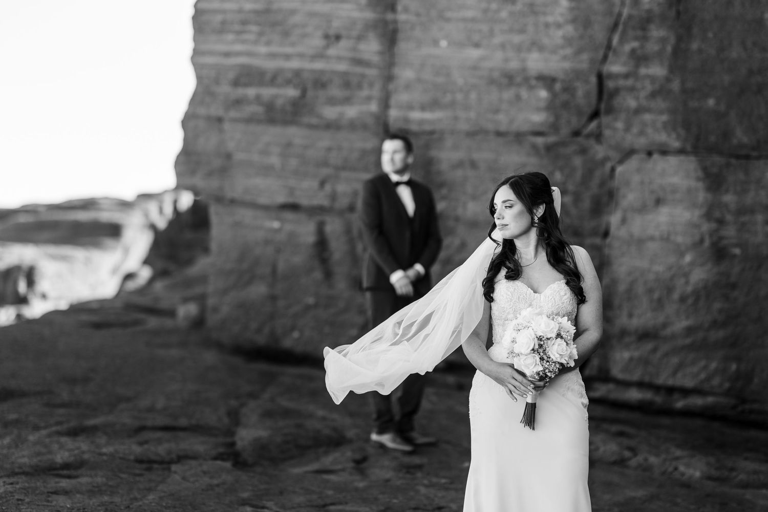 Black and white wedding photo series showing intimate moments between a couple against a stone wall backdrop.