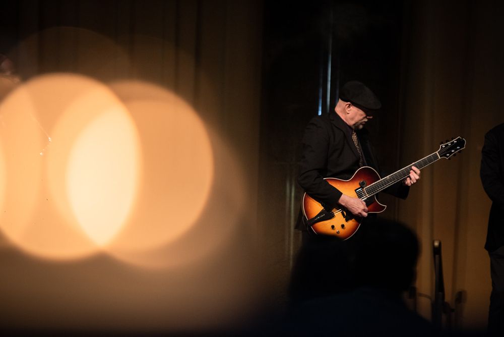 Silhouettes of musicians performing on a dimly lit stage with warm spotlights.