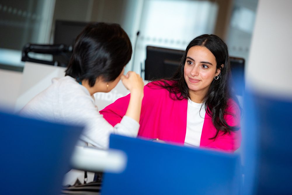 Professional wearing bright pink blazer sits at desk in modern office environment.