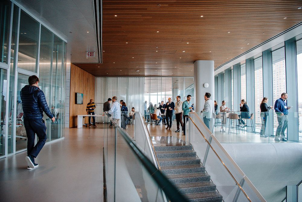 Modern office hallway with glass walls and natural light showing people walking through the corridor.