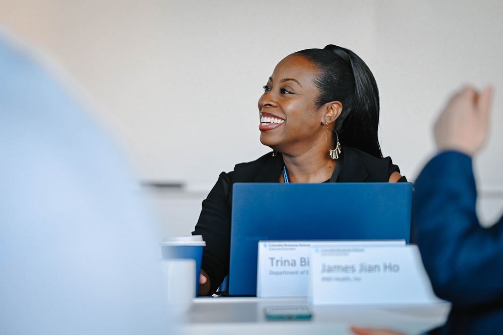 Professional at a conference table smiles warmly while seated behind a blue folder during a business meeting.
