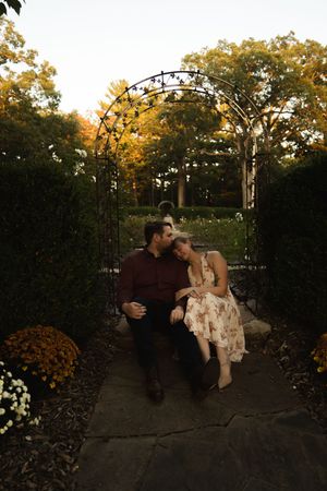 A couple shares a sweet moment on a garden bench under an ornate metal arch.