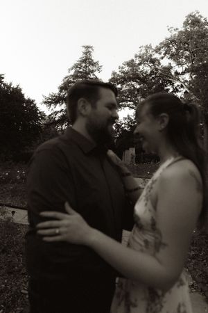 A black and white portrait of a couple sharing a joyful embrace outdoors.